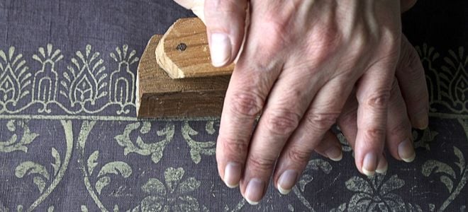 two hands pressing a patterned stamp down onto fabric