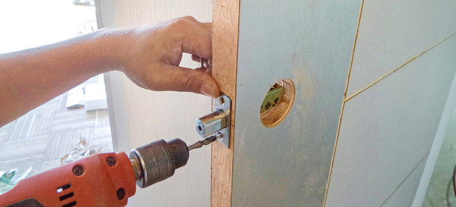 hand and drill installing a deadbolt lock