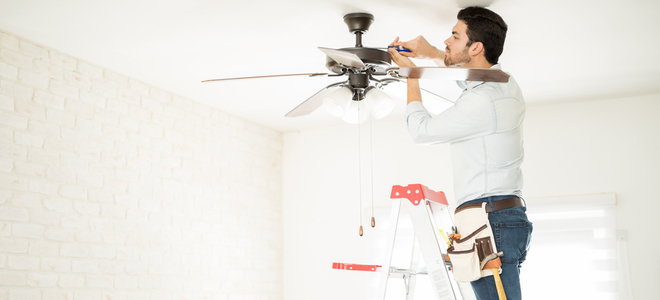 Man on a ladder repairing a ceiling fan