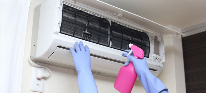 gloved hands cleaning AC unit with spray bottle