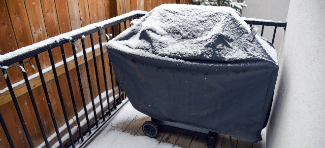 covered grill with light snow on a deck porch