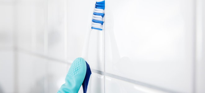 gloved hand cleaning bathroom tile grout with a toothbrush