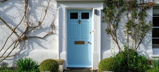 pretty blue door with molding on white house with rose bushes