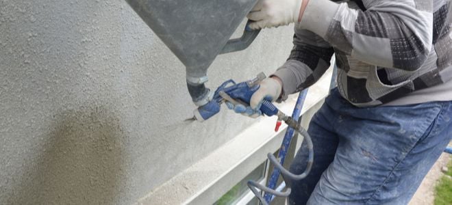 worker using hopper spray gun to apply texture to exterior wall