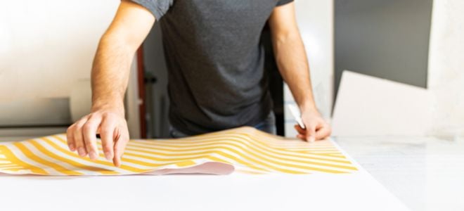 person spreading out peel and stick wallpaper with yellow line design