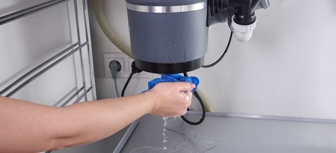 hand with rag under a leaking garbage disposal
