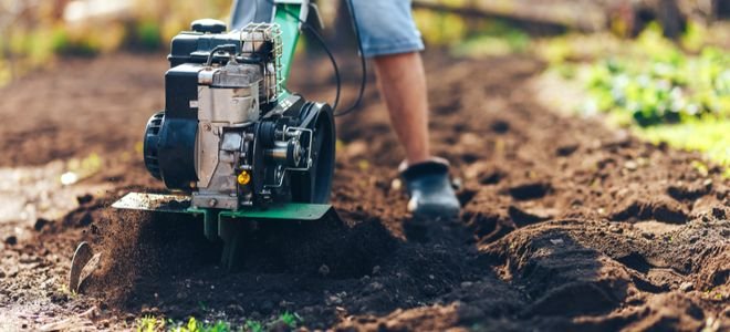 person pushing large green rototiller over garden soil