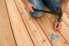 A worker nailing deck boards with a hammer and nails.