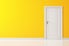 A white, interior door set into a yellow wall.