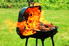 A portable barbeque outdoors with the large flames of a flash fire coming out.