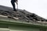 A construction worker removing shingles from a roof. 