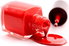 A bottle of red nail polish spilling onto a white surface. 