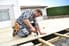 A handyman constructing a wood deck and using an impact driver. 