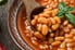 bowl of cooked beans with basil, hot pepper and wooden spoon