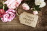 A gift tag saying "Happy Mother's Day!" against a background of wood and pink roses. 