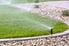 sprinkler spraying water on lawn surrounded by rock bed
