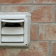 white dryer vent mounted in a brick wall