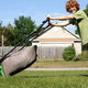 A red-headed boy mowing the lawn with a bagged push mower.