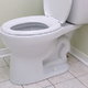 A white, porcelain toilet in the corner of a bathroom.