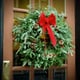 An evergreen wreath with a red bow hanging on a door.