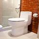 A toilet in a bathroom with a brick wall and a shower stall.
