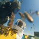 A couple of beekeepers working around a hive with bees flying into the blue sky.