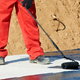 A worker rolling roofing tar on a flat roof.
