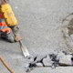 person in protective gear using a jackhammer to remove a concrete walkway