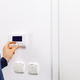 A man adjusting a thermostat on a white wall. 