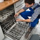 A man removing the drain from a dishwasher.