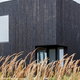 small building in grassy field with charred wood exterior