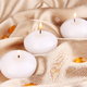 Small, white tea light candles on gold satin fabric.