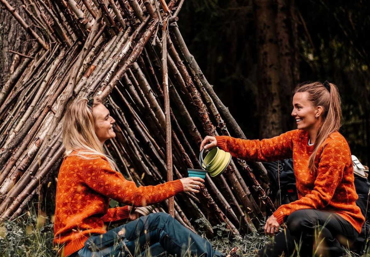 Two women share hot tea wrapped up in cozy sweaters while enjoying the great outdoors.