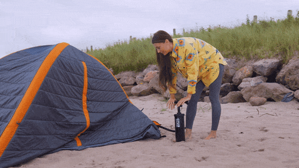 Woman inflates her Crucoon tent on a sandy beach. 