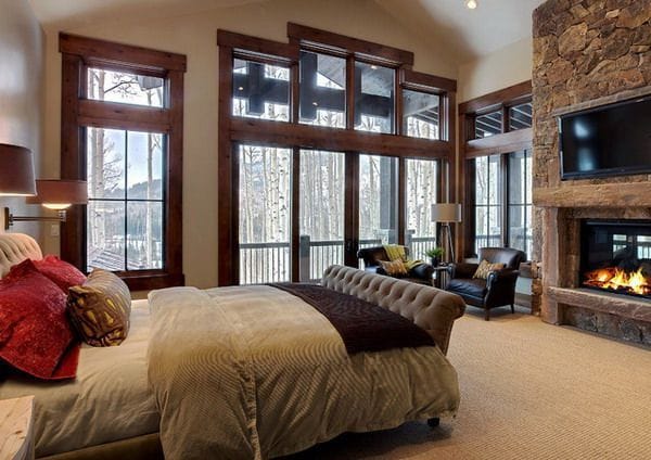 This cabin-style bedroom features lots of dark browns, and it even boasts its own fireplace under a flat-screen TV!