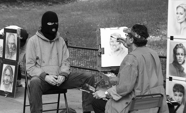 Elusive street artist Banksy gets his portrait drawn while wearing a black ski mask. 