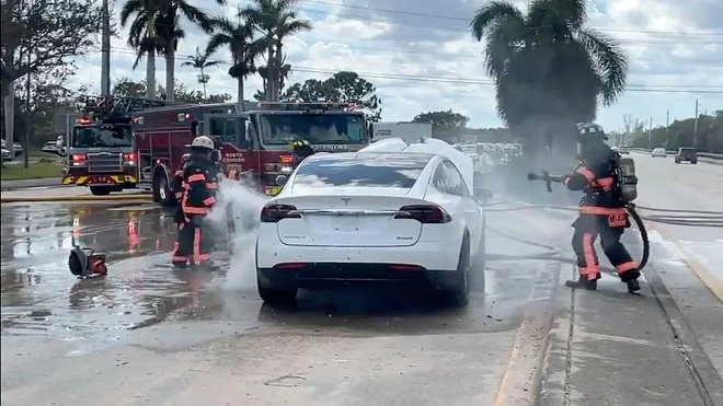 Firefighters hose down a burning Tesla EV in the aftermath of Hurricane Ian.