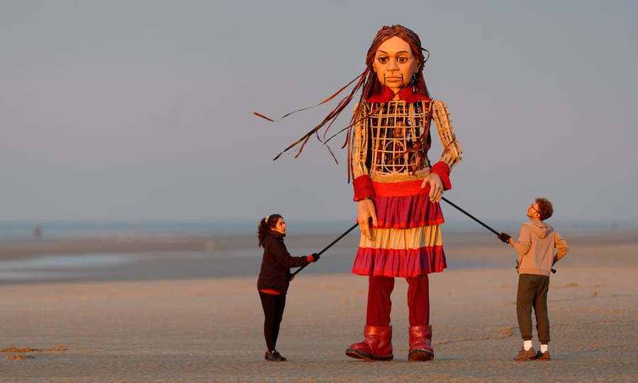 Volunteers hold up the Little Amal puppet on a European beach.