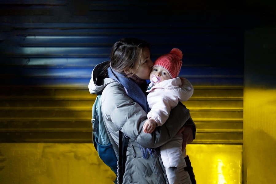 Ukrainian mother holds her baby in front of a wall painted with the colors of Ukraine's flag.