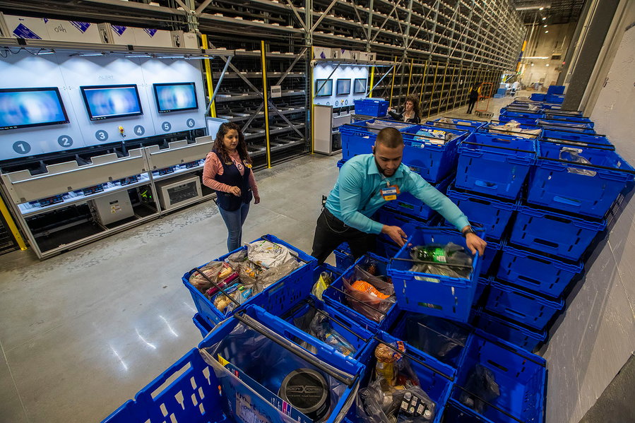 Walmart employees sort baskets full of food to meet customers' online grocery orders.