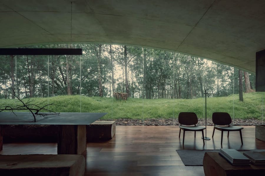 The Hill in Front of the Glen's minimalist open plan living and dining areas, with views of the surrounding forest through the large semicircle opening in the background.
