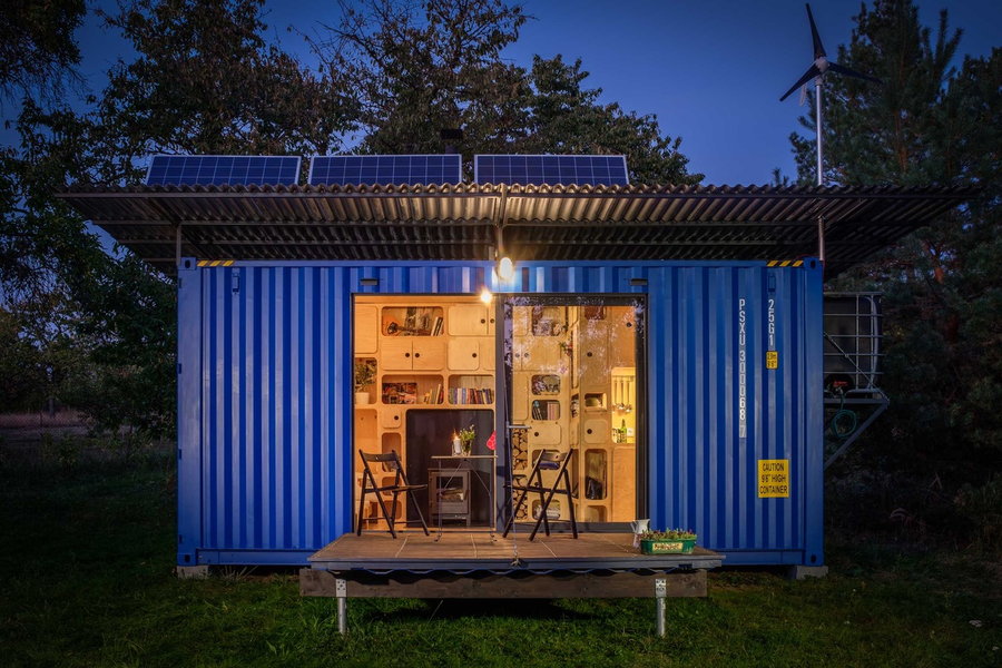 The cozy Gaia Off-Grid Container House emits a warm glow in the evening.