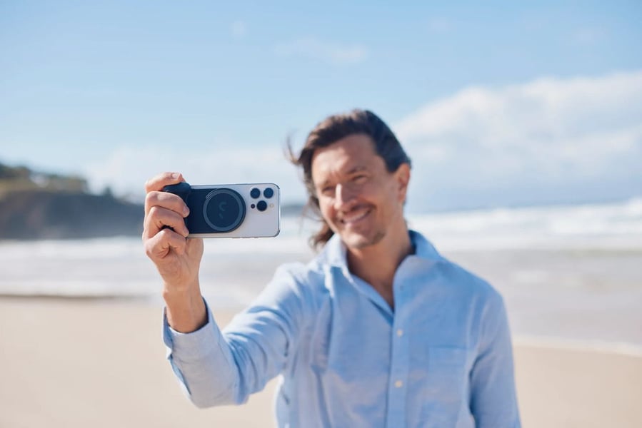 Man holds his phone with the ShiftCam SnapGrip to snap a pic on the beach.