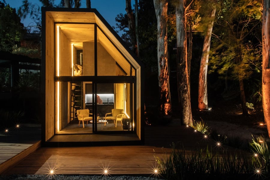 Cabana Portable Tiny House emits a warm nighttime glow through its large glass windows.