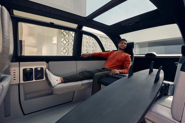 Man lounges in the Canoo's backseat using the car's hidden pull-out seats.