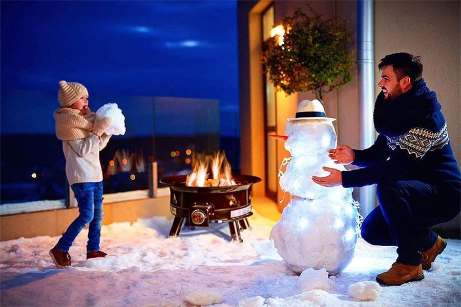 Couple plays in the snow by their Outland Living Firebowl Propane Gas Fire Pit.