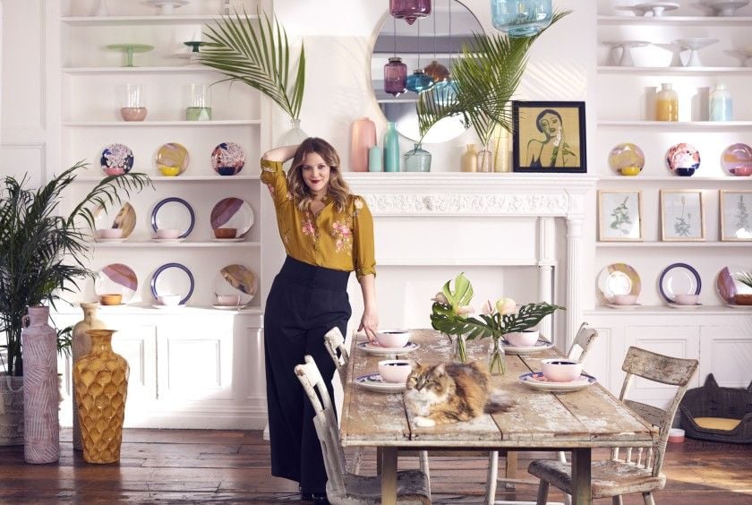 Drew Barrymore stands over a whimsical yet elegant dining space adorned with her 