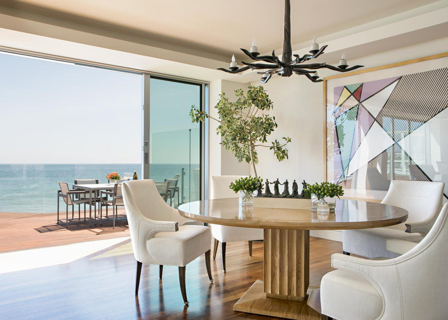 The spacious white dining area inside the metallic Malibu beach house, with operable glazing and the Pacific visible in the background.