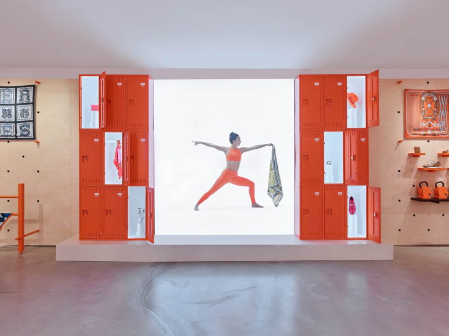 Bright orange lockers flank a lit-up picture of a woman performing a yoga pose inside a 