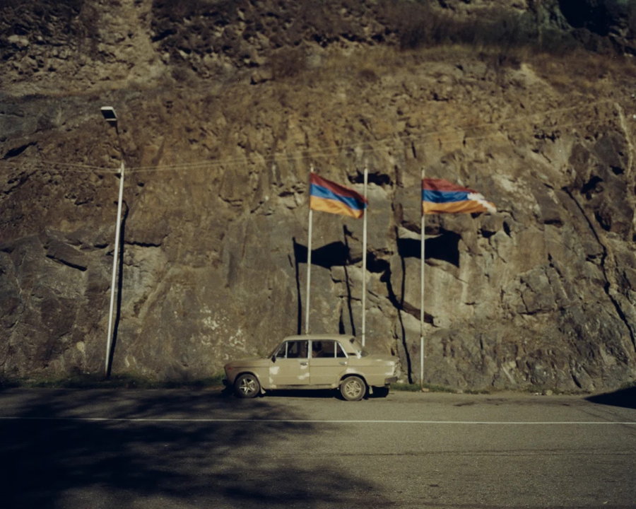 Old Soviet-era Lada car parked in front of two Armenian flags, photographed by Alex Nazari.
